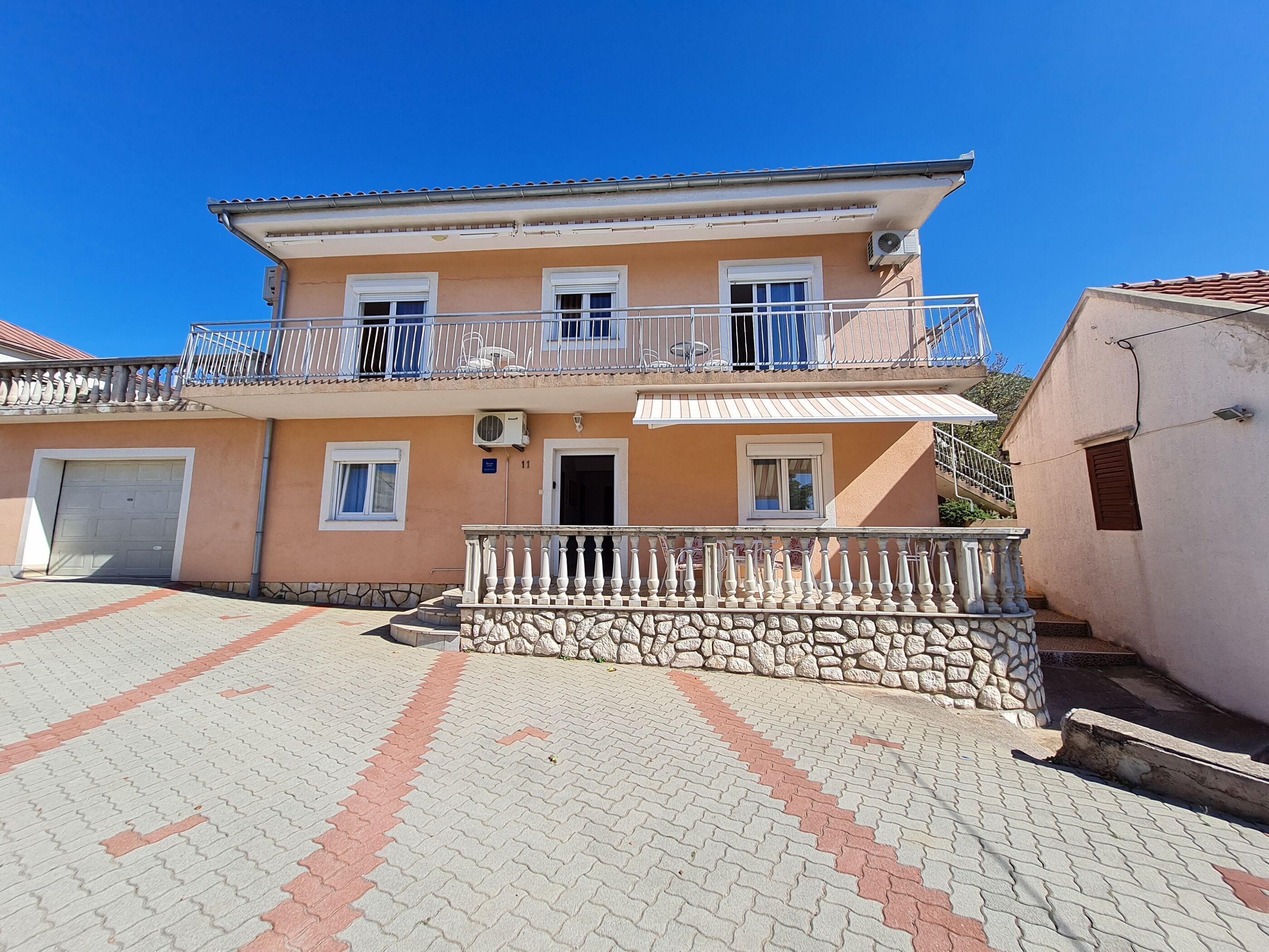 A two-story building with a balcony, a garage, and a paved courtyard.