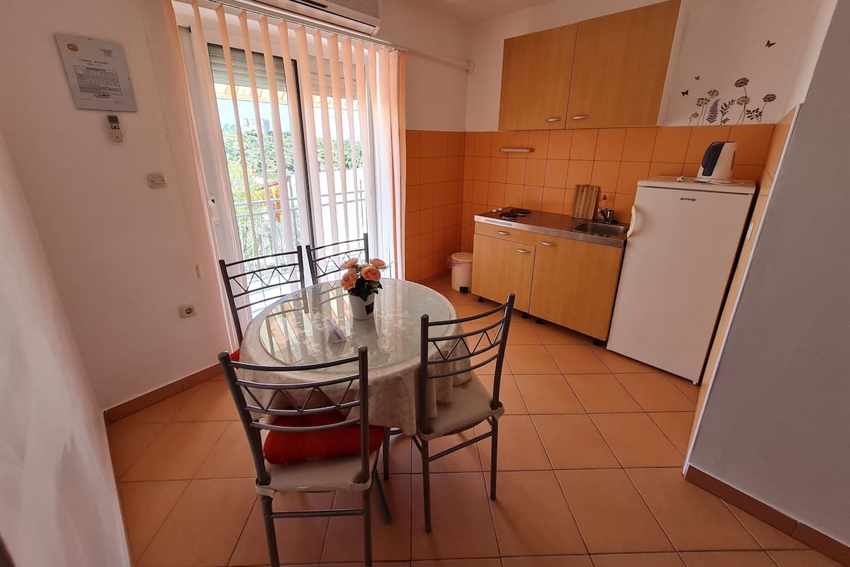 Une cuisine compacte équipée d’un réfrigérateur, d’un évier et d’un petit plan de travail. On y trouve une table à manger avec des chaises et un vase de fleurs.