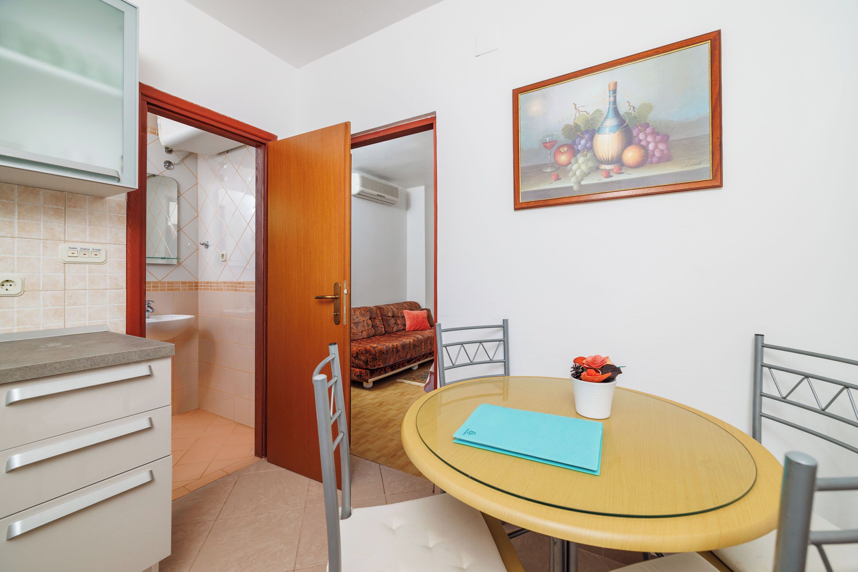 A compact living space with a kitchenette, a dining area with a round table, and a painting on the wall.