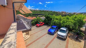 Zona residencial con camino pavimentado, coches aparcados y un balcón con vistas a una colina.