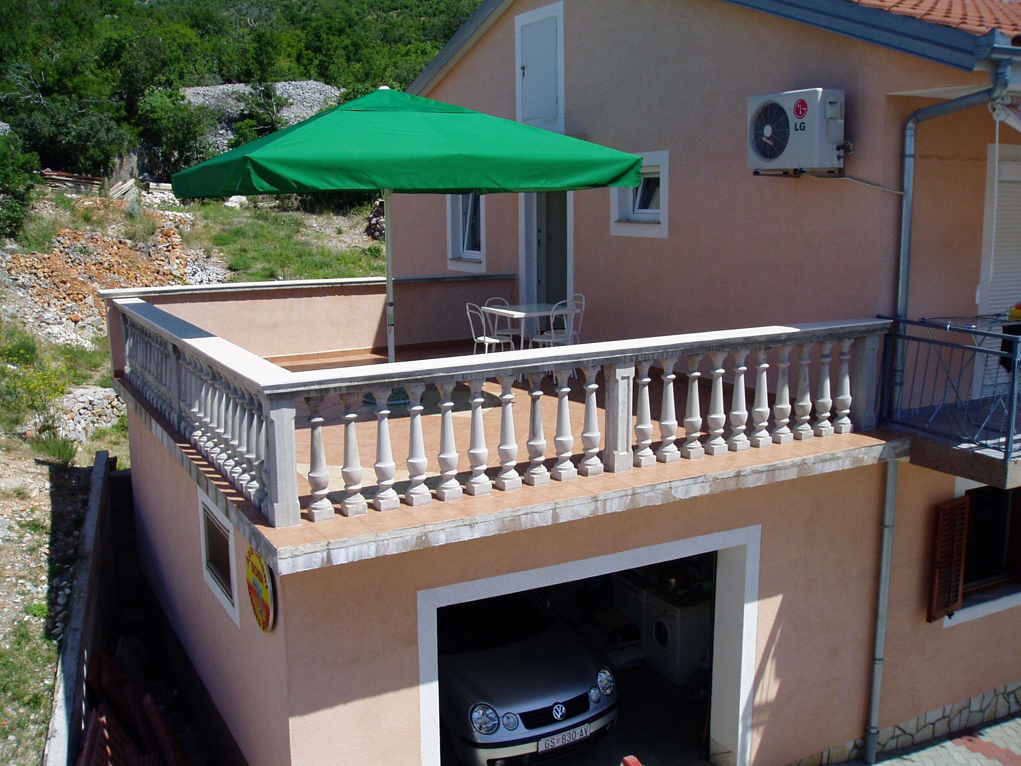 A building with a balcony, a green umbrella, and a parked car.