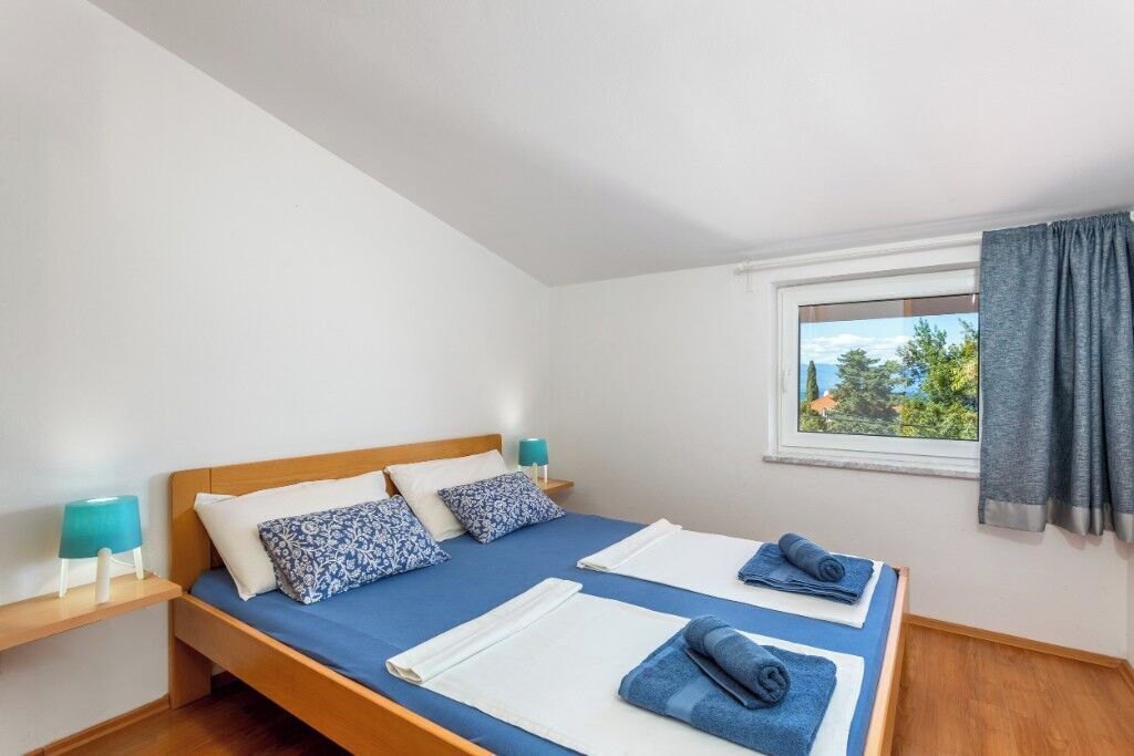 Une chambre à coucher avec un lit, deux tables de chevet, une fenêtre avec des rideaux et une vue sur la verdure à l’extérieur.