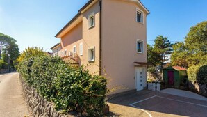 Ein zweigeschossiges Gebäude mit einer beigen Fassade, einer kleinen Veranda und einem grünen Schuppen im Hintergrund.