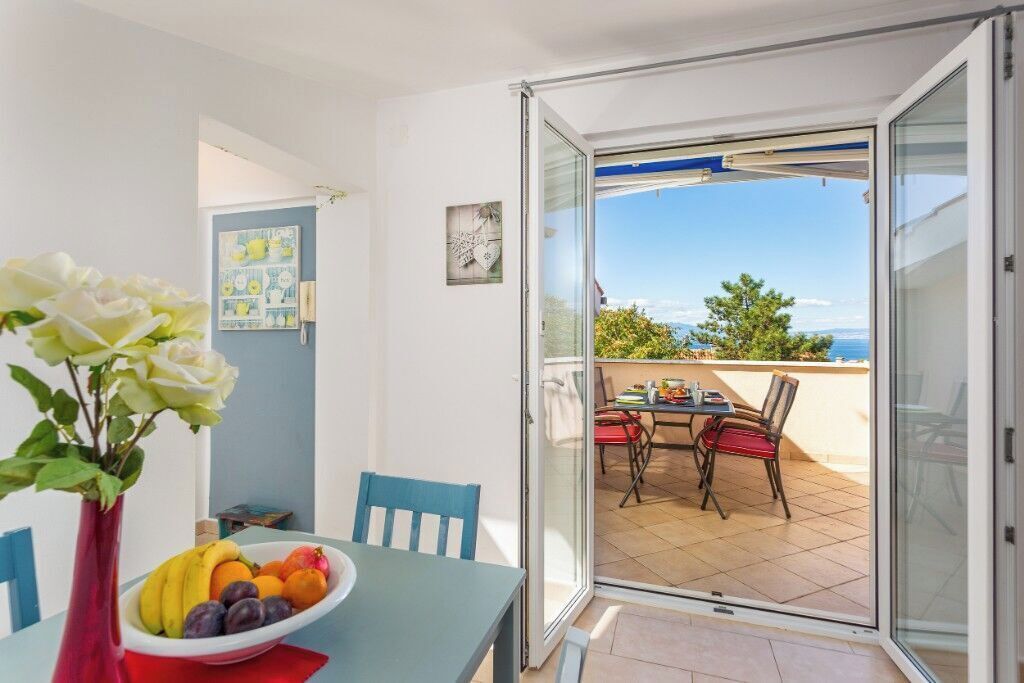 Un balcon avec une table et des chaises, un vase rempli de fleurs et un saladier de fruits.