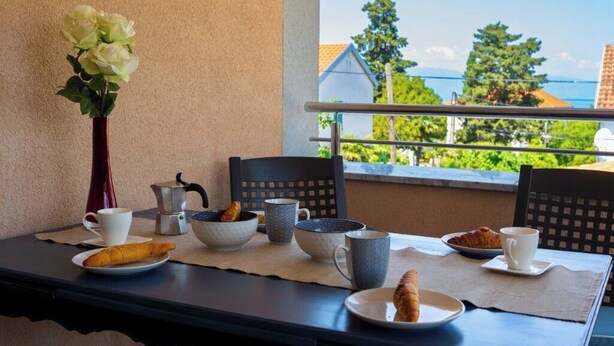 Ein Frühstückstisch mit Croissants, Kaffee und einer Blumenvase auf einem Balkon mit Blick auf eine schöne Aussicht.