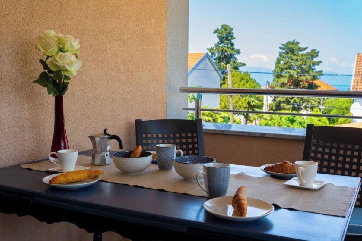 A breakfast setup with croissants, coffee, and a vase of flowers on a balcony overlooking a scenic view.