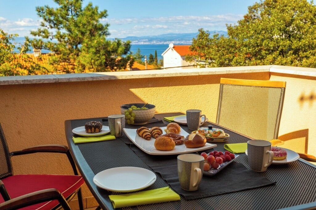 Ein Frühstückstisch mit Stühlen auf einem Balkon, Blick auf das Meer und die Berge.