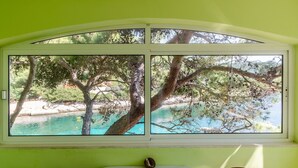 Ein Zimmer mit einem großen Fenster mit Blick auf türkisfarbenes Wasser und Bäume.