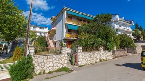 Un edificio residenziale a più piani con balconi, un muro in pietra e un cielo azzurro intenso.