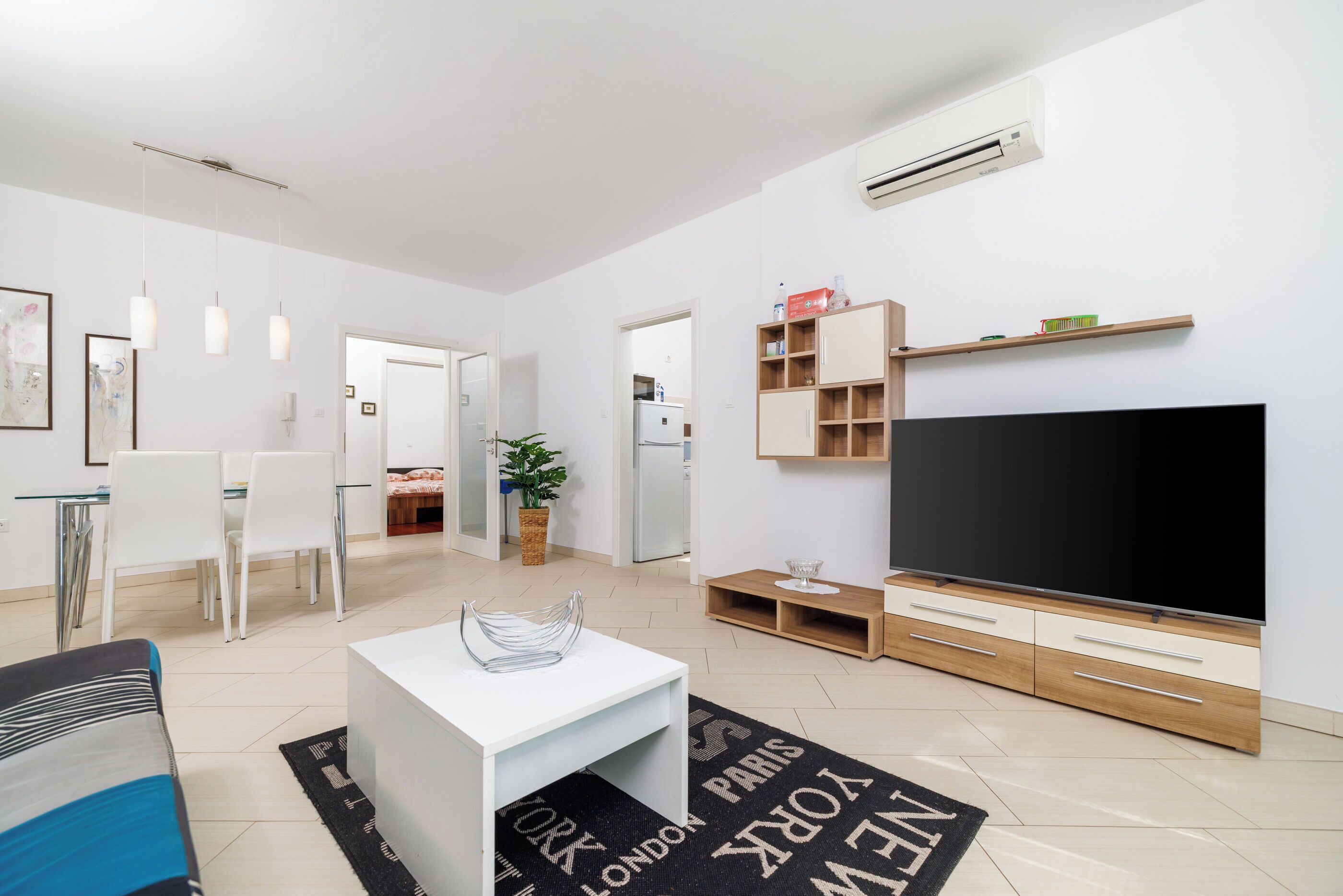 Una sala de estar moderna con televisor de pantalla plana, comedor con sillas, sofá y mesa de centro.