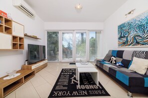A modern living room with a flat-screen TV, a sofa, a coffee table, and a large window with blinds. - Apartment Villa Sara (Crikvenica)