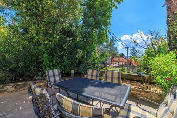 Eine Terrasse im Freien mit einem Metalltisch und -stühlen, umgeben von üppiger Bepflanzung und einer Steinmauer.