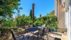 An outdoor patio with a table and chairs, surrounded by greenery and a tall palm tree. - Apartment Villa Sara (Crikvenica)