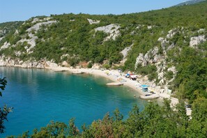 A coastal beach with clear turquoise waters, a sandy shore, and rocky cliffs. - Apartments Badnje (Crikvenica)