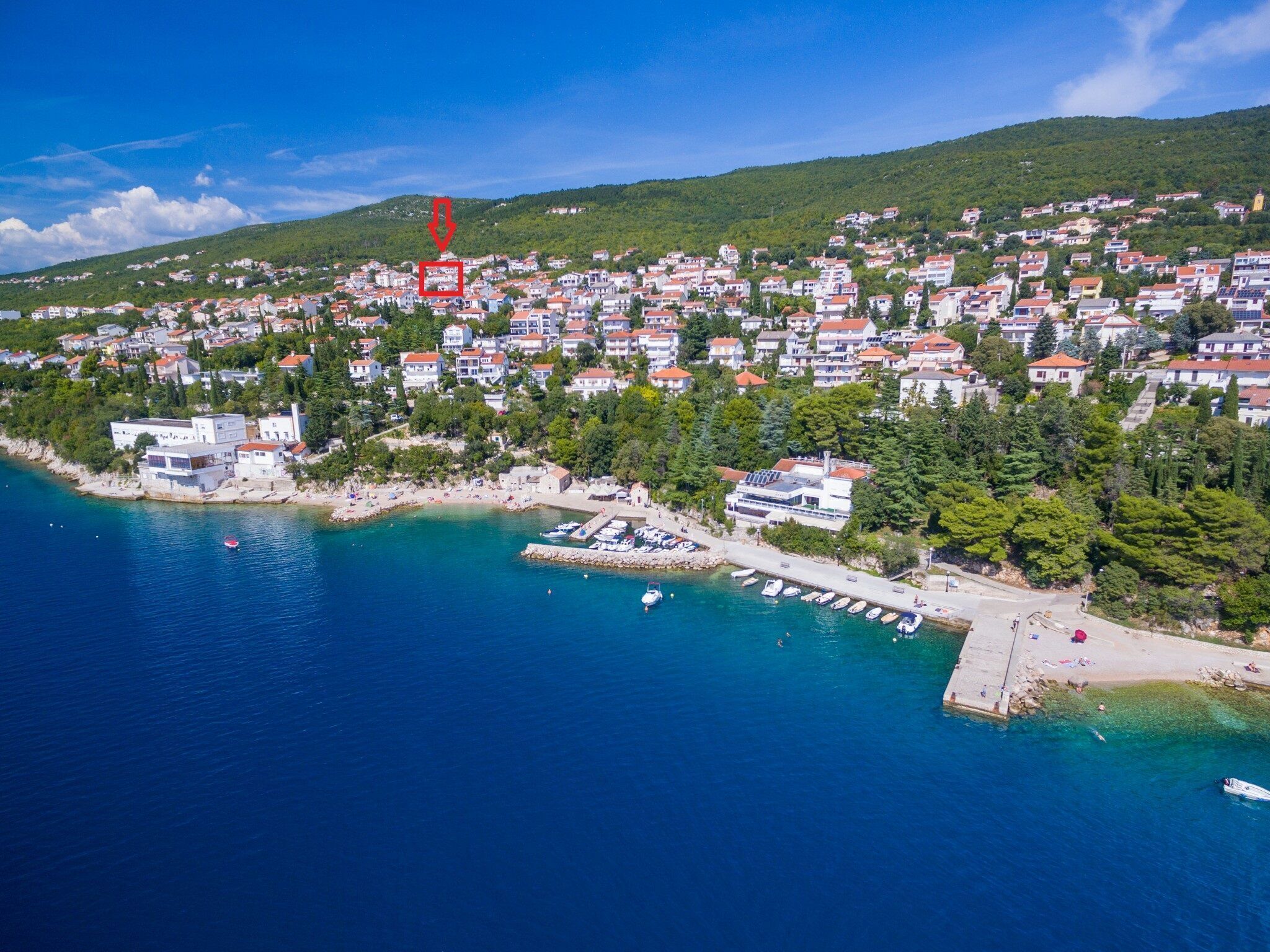 A coastal town with a marina, houses, and a hill in the background.