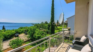 Un balcon doté de meubles en osier et d’une antenne parabolique, offrant une vue sur un jardin luxuriant et une étendue d’eau.