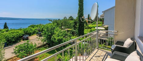 A balcony with wicker furniture and a satellite dish, overlooking a lush garden and a body of water.