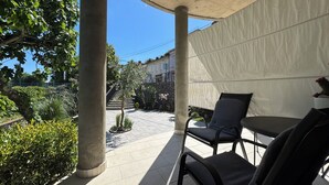 Un espacio al aire libre con patio, sillas, una mesa y vistas a una calle residencial.