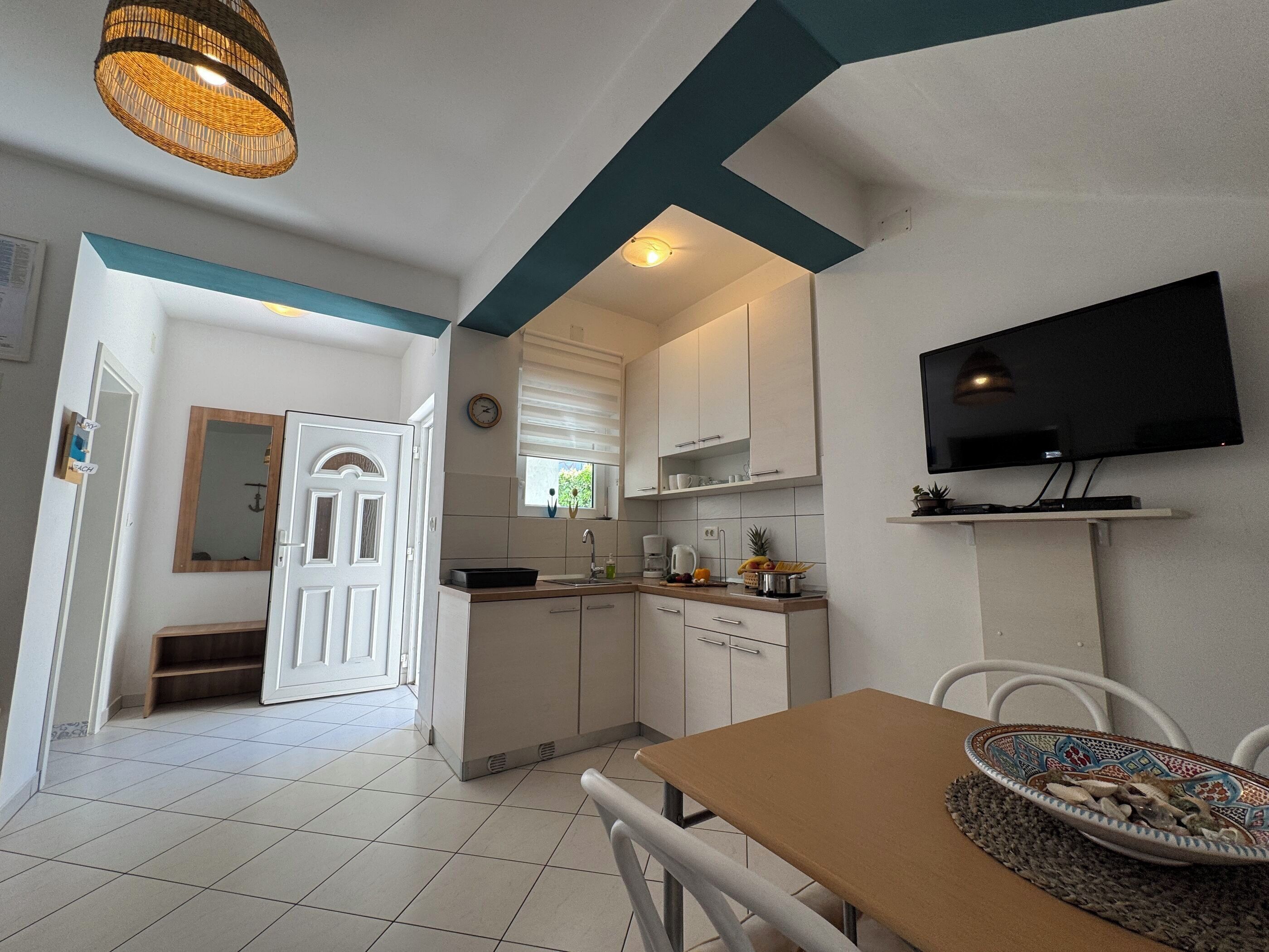 Una cocina moderna con armarios blancos, una mesa de comedor y un televisor de pantalla plana.