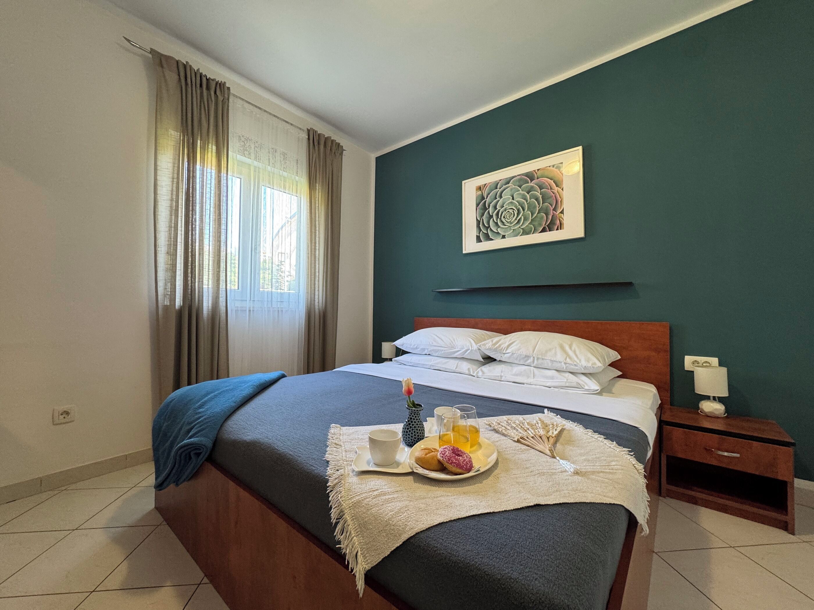 A neatly made bed with a blue blanket, a bedside table with a lamp, and a wall-mounted artwork.