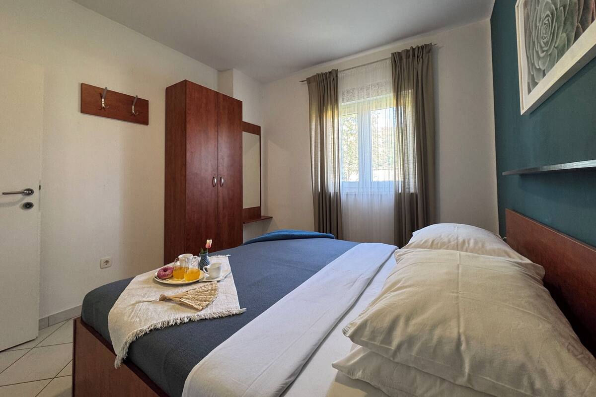 A bedroom with a bed, a wardrobe, a window with curtains, and a wall-mounted picture.