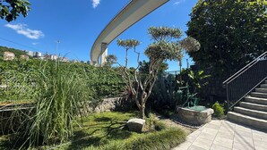 Un área ajardinada con un sendero curvo, un banco de piedra y una escalera.