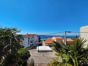 Un quartier résidentiel offrant une vue dégagée sur la mer, avec des bâtiments aux toits recouverts de tuiles rouges et un immeuble blanc doté d’un balcon.