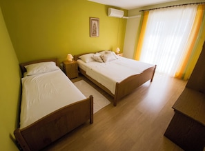 A room with two wooden beds, a nightstand with a lamp, a wall-mounted air conditioner, and a window with curtains. - Apartments Cacija (Okrug)