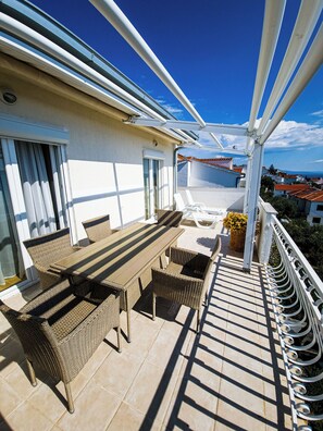Ein Balkon mit Korbmöbeln, Fliesenboden und Blick auf das Meer und die Gebäude.