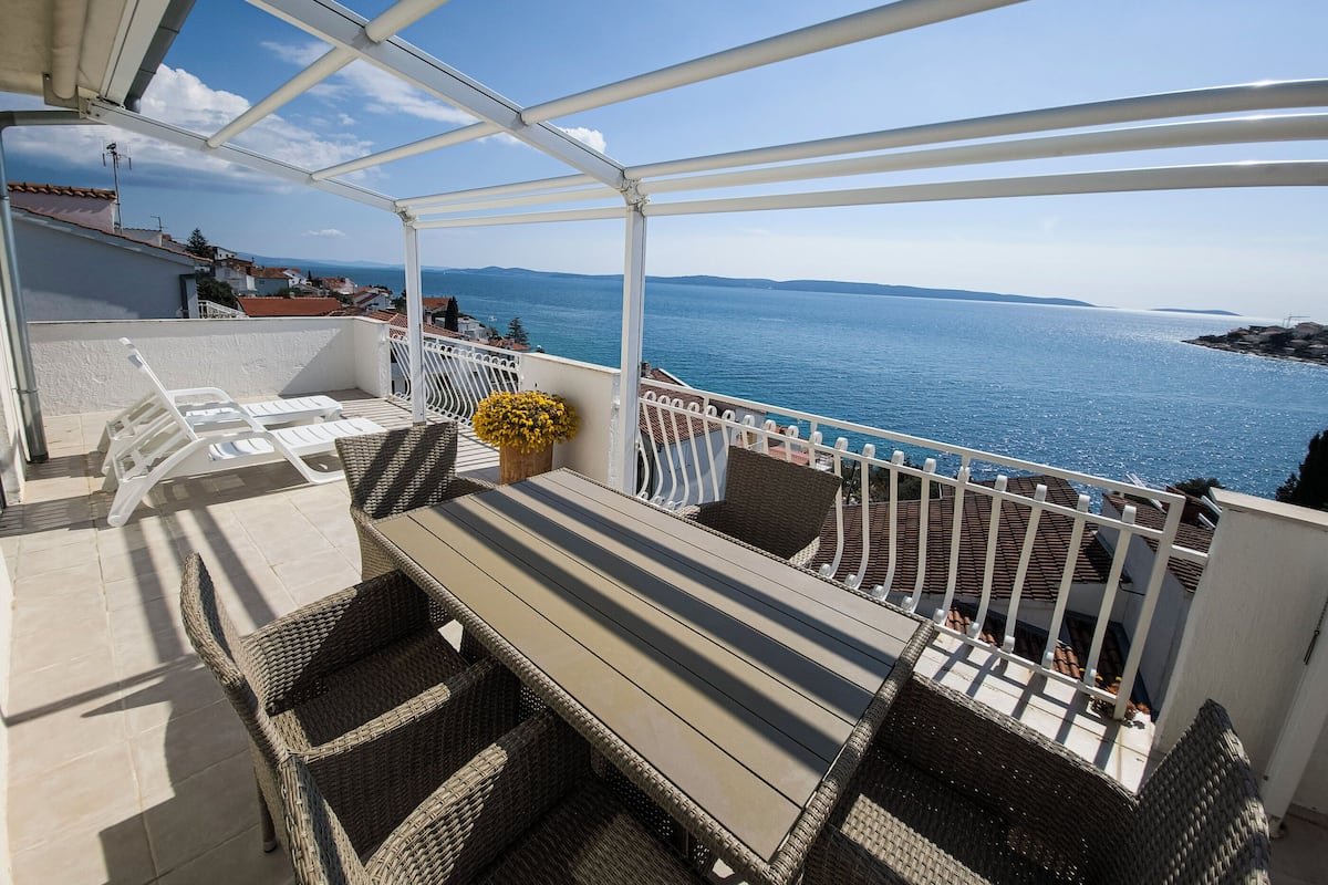 A balcony with a white railing, wicker furniture, and a view of the sea.