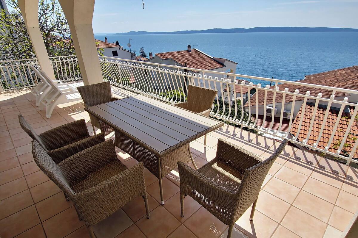 A terrace with a table and wicker chairs, overlooking a coastal view.