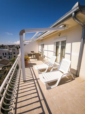 A balcony with white lounge chairs, a table, and a potted plant. - Apartments Cacija (Okrug)