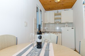 Una mesa de comedor con una botella de vino y dos copas, techo de madera y armarios blancos en una cocina.
