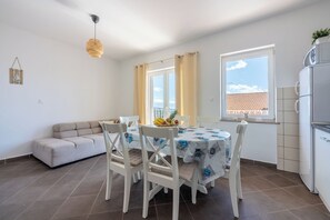 A modern kitchen with a dining area, white furniture, and a view of the city. - Apartments Trossana (Crikvenica)