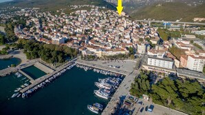 Luftaufnahme einer Küstenstadt mit einer Marina, einem dicht bebauten Wohngebiet und einem markanten gelben Pfeil, der auf einen bestimmten Ort zeigt.