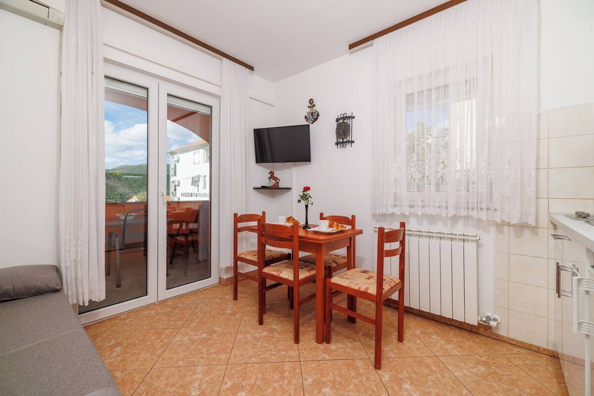 Ein Essbereich mit Tisch und Stühlen, einem an der Wand befestigten Fernseher und Blick durch eine Schiebetür.