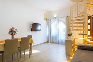 Una sala de estar moderna con comedor, un televisor de pantalla plana montado en la pared, una escalera y un ventanal con cortinas traslúcidas.