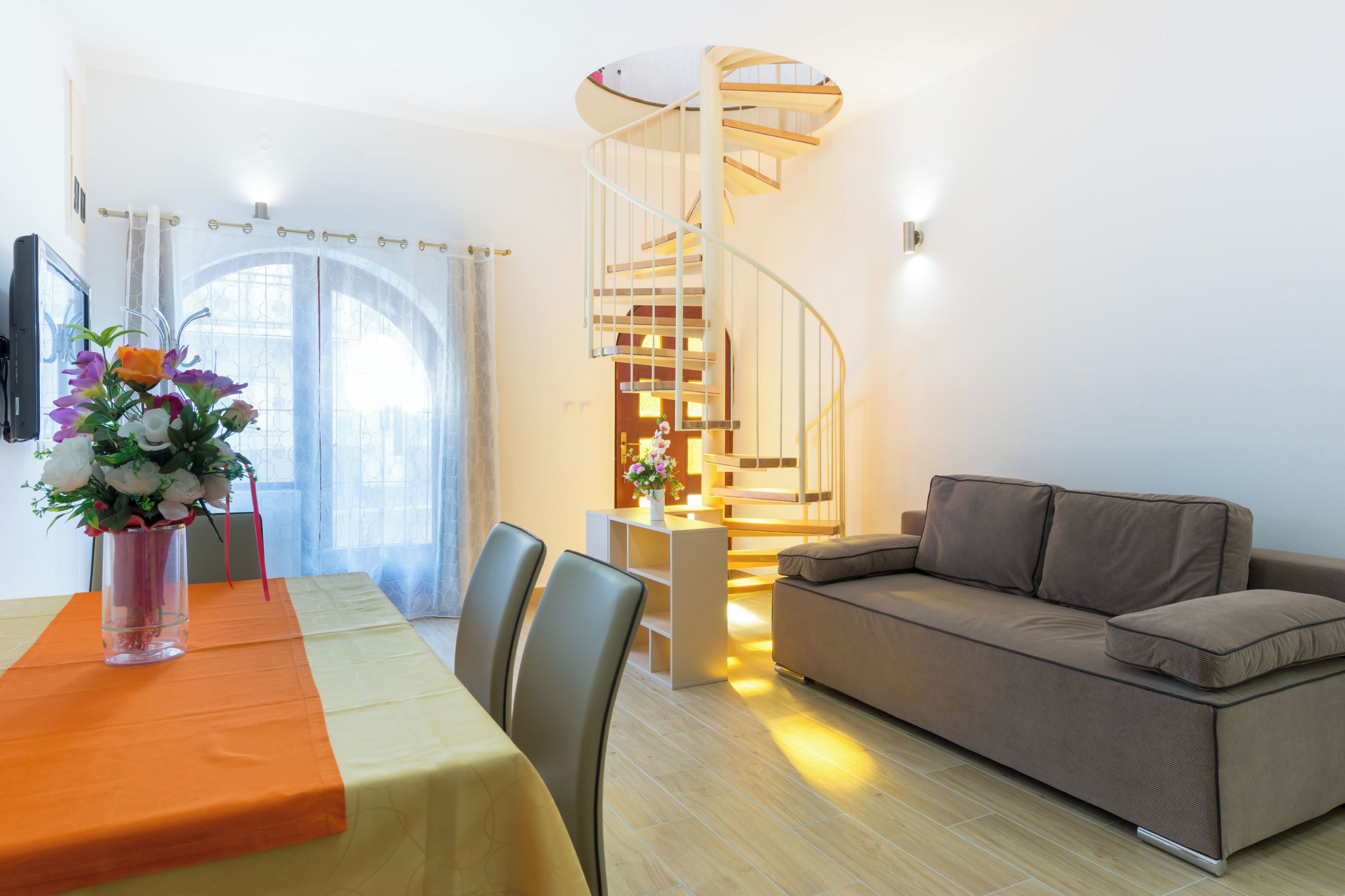Ein modernes Wohnzimmer mit Wendeltreppe, einer Couch und einem Essbereich mit Tisch und Stühlen.