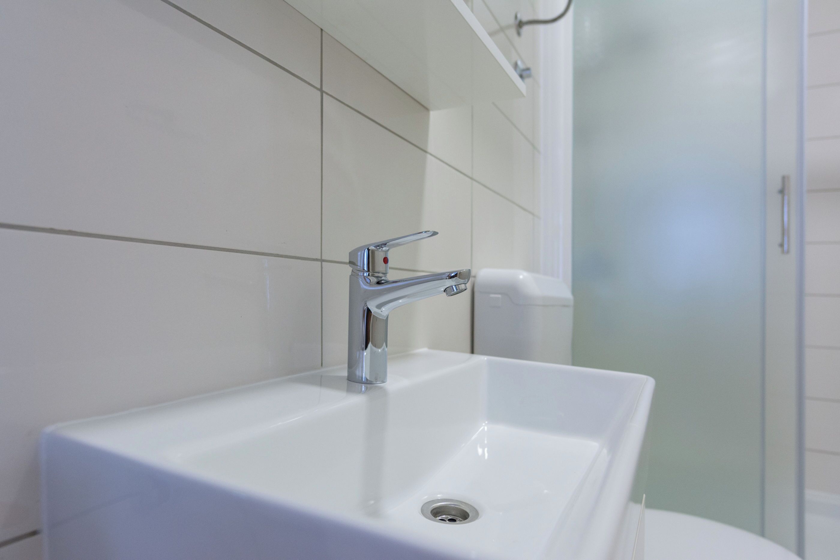 Ein Badezimmer mit weißem Waschbecken, chromfarbenem Wasserhahn und einer Duschkabine aus Glas.
