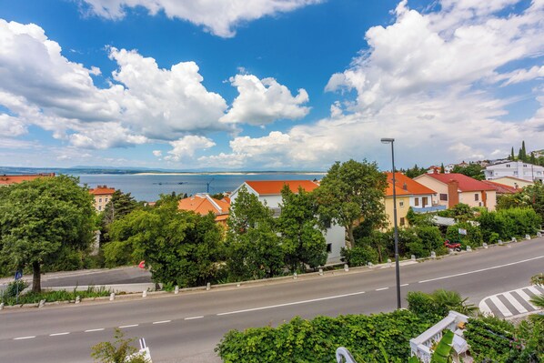 A coastal town with a wide road, green trees, and buildings with red roofs. - Apartments Marijana (Crikvenica)