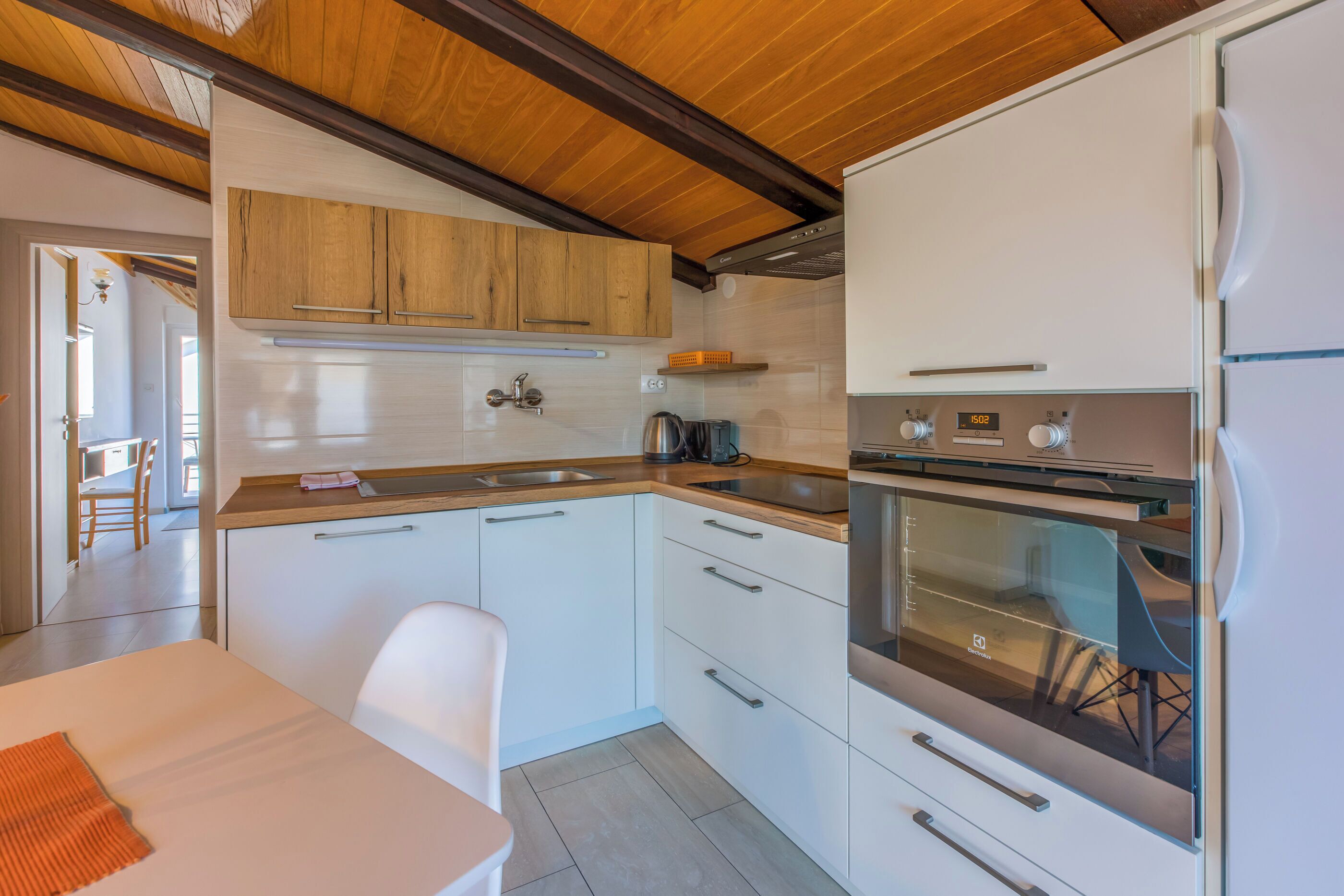 A modern kitchen with white cabinets, a stainless steel oven, and a wooden ceiling.