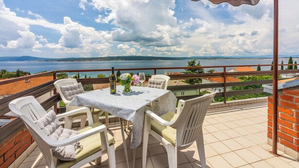 Une terrasse avec une table dressée pour deux personnes, offrant une vue sur une étendue d’eau et sur la terre ferme au loin.