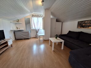 Un soggiorno moderno con pavimento in legno, un divano nero, un tavolino da caffè bianco e una televisione su un mobile in legno.