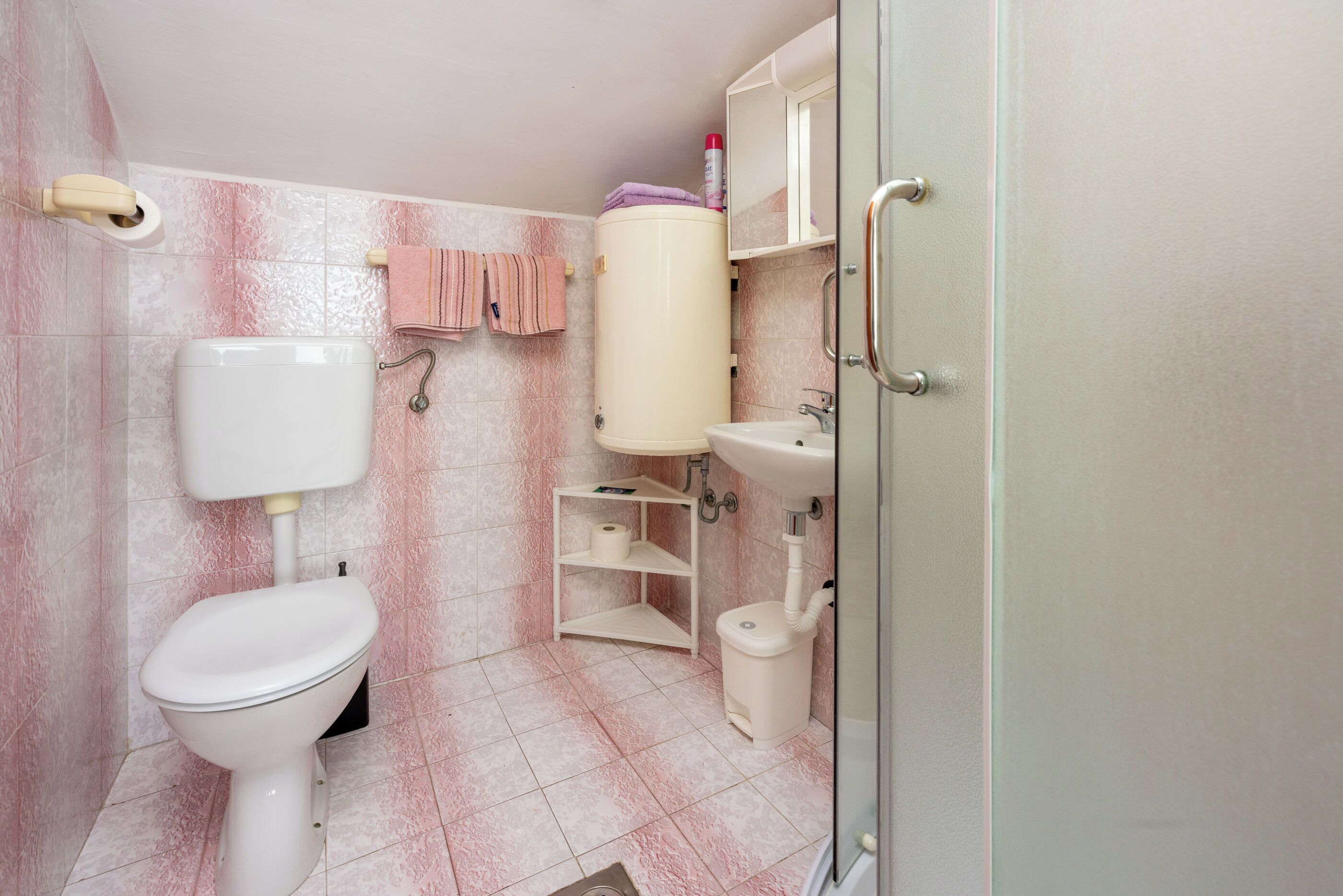A bathroom with a toilet, sink, and storage shelves.