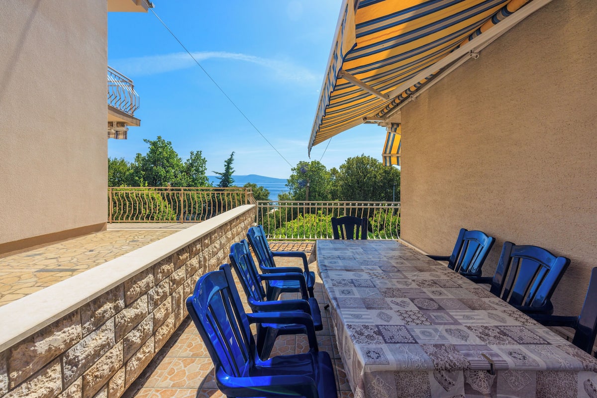 Eine Terrasse mit Tisch und Stühlen, Blick auf Grünflächen und Berge, sowie ein Balkon mit Geländer.