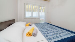 A hotel room with a bed, two rolled towels, a patterned bedspread, and a window with curtains. - Apartments Antonio (Crikvenica)