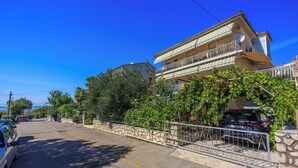 A two-story building with balconies, a stone wall, and parked cars. - Apartments Antonio (Crikvenica)