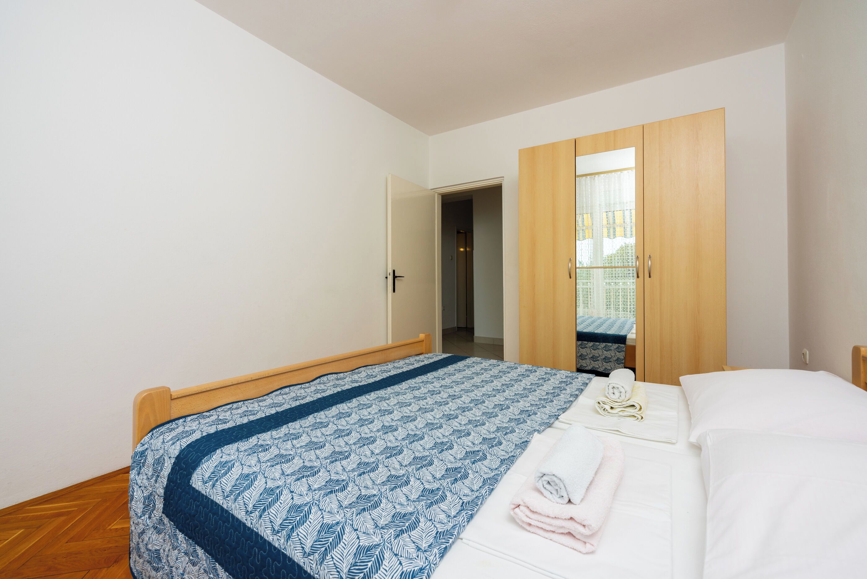 A bedroom with a wooden bed, a blue patterned bedspread, a white pillow, and a wooden wardrobe.