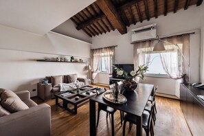 Un soggiorno moderno con divano, tavolino da caffè e tavolo da pranzo. Si vede una TV, una lampada e una finestra con tende.