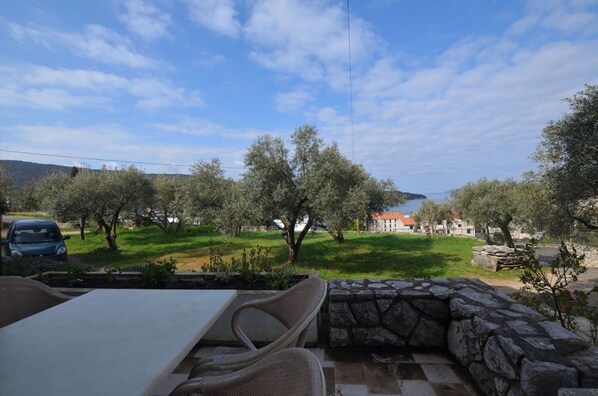 A patio with a stone wall, a table, and a chair. - Apartments Ljubomir (Cres)